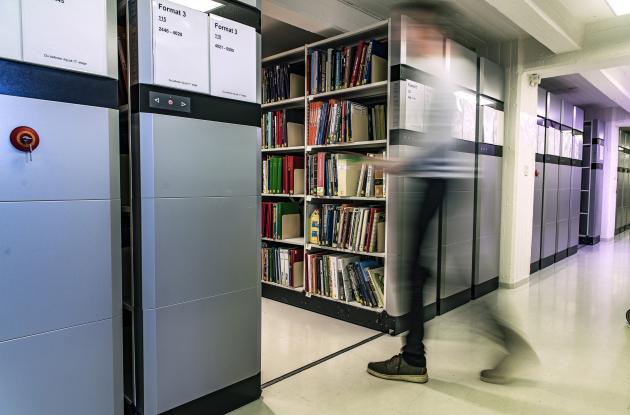 Employee picks up materials between compact shelves