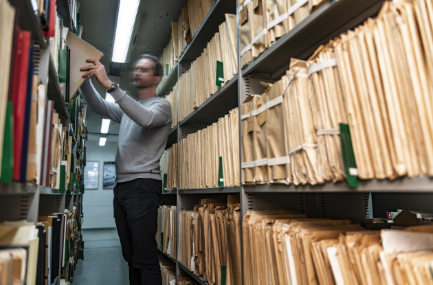 Person between shelves with archive folders and books